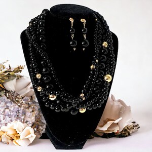 Peut inclure: Un collier multi-rangs de perles noires avec des accents dorés. Le collier est présenté sur un support en velours noir. Des boucles d'oreilles assorties sont également incluses.
