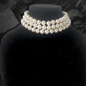May include: A triple strand pearl choker necklace on a black velvet mannequin bust.