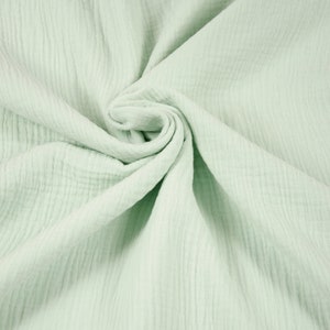 Könnte beinhalten: Nahaufnahme eines hellgrünen Stoffes mit strukturierter Oberfläche. Der Stoff ist in einer Spirale angeordnet, die die Falten und die weiche, gekräuselte Textur zeigt. Die Farbe ist ein blasses, gedämpftes Grün, das an Minze oder Salbei erinnert.