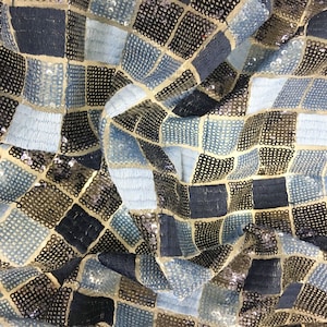 Könnte beinhalten: Ein Stoff mit einem geometrischen Muster aus blauen, schwarzen und goldenen Pailletten. Die Pailletten sind in einem Gittermuster angeordnet, wodurch ein schimmernder Effekt entsteht.