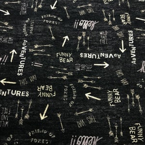 Könnte beinhalten: Schwarzer Stoff mit einem weißen und goldenen Druck von Pfeilen, Wörtern und Phrasen. Die Wörter beinhalten "Wild and Free", "Funny Bear", "Friend of the Forest" und "Adventures this way".