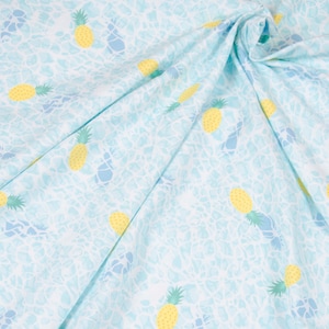 Könnte beinhalten: Ein hellblauer Stoff mit einem weißen und hellblauen Muster mit gelben Ananas. Der Stoff ist gefaltet und drapiert.