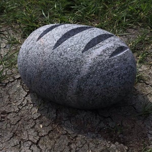 May include: A gray stone sculpture shaped like a loaf of bread with three grooves carved into the top.