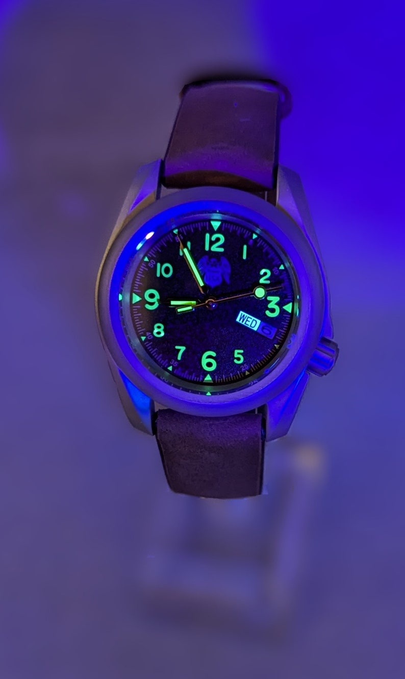 May include: A black watch with a silver case and a brown leather band. The watch face has luminous green hands and markers, and the day of the week is displayed as "WED".