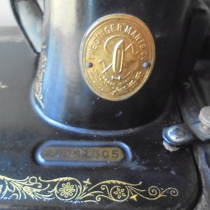 Op de afbeelding: Een zwarte Singer naaimachine met een gouden metalen plaat waarop "The Singer Mfg Co." en een serienummer "47091305" staat.