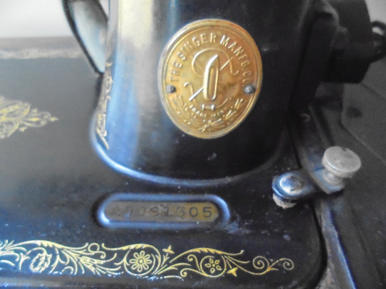 Op de afbeelding: Een zwarte Singer naaimachine met een gouden metalen plaat waarop "The Singer Mfg Co." en een serienummer "47091305" staat.