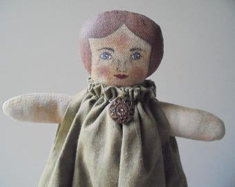 May include: A handmade rag doll with a painted face, brown hair, and a green dress. The doll has a button on the front of the dress.