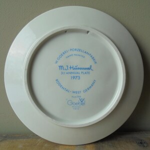 May include: A white porcelain plate with blue text and a circular design. The text includes "W. Goebel - Porzellanfabrik", "M.J. Hummel 39 Annual Plate 1973", and "Rodental-West Germany". The plate is hand-painted.
