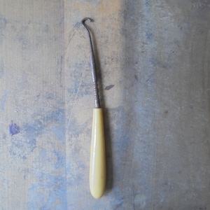 May include: A vintage shoe horn with a cream-colored plastic handle and a metal hook.