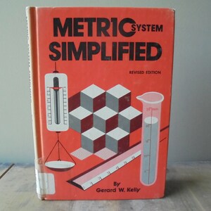 May include: A red book titled "Metric System Simplified" with a revised edition label. The cover features illustrations of a scale, a thermometer, a ruler, a graduated cylinder, and a cube pattern.