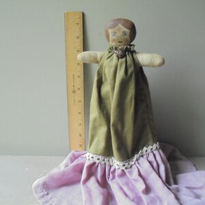 K&ouml;nnte beinhalten: Eine Vintage-Stoffpuppe mit bemaltem Gesicht und braunen Haaren. Die Puppe tr&auml;gt ein gr&uuml;nes Kleid mit wei&szlig;er Spitzenborte und einen rosa Rock.