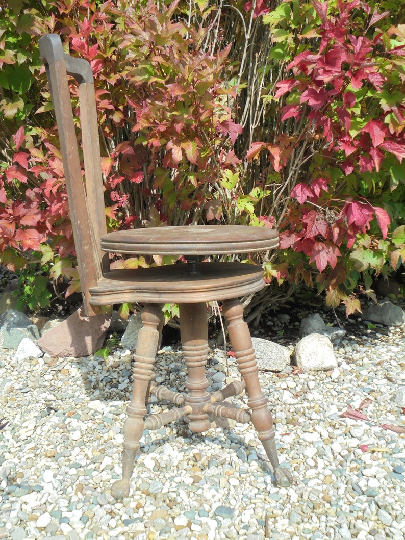 Pu&ograve; includere: Uno sgabello girevole in legno con un sedile rotondo e uno schienale alto. Lo sgabello ha una finitura marrone scuro e intagli intricati sulle gambe. Lo sgabello &egrave; seduto su un letto di ghiaia.