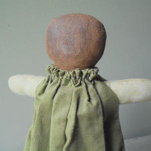K&ouml;nnte beinhalten: Eine handgemachte Stoffpuppe mit einem braunen Stoffkopf und einem gr&uuml;nen Stoffkleid. Die Puppe hat ein schlichtes, rustikales Aussehen.