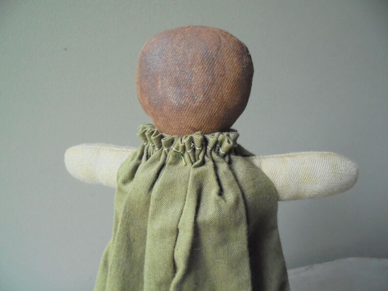K&ouml;nnte beinhalten: Eine handgemachte Stoffpuppe mit einem braunen Stoffkopf und einem gr&uuml;nen Stoffkleid. Die Puppe hat ein schlichtes, rustikales Aussehen.