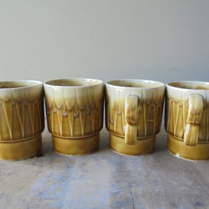 May include: Set of four brown and white ceramic mugs with a geometric pattern. The mugs have a wide base and a rounded top.
