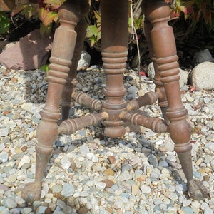 Pu&ograve; includere: Uno sgabello di legno con piano rotondo e tre gambe. Le gambe sono tornite e hanno un design decorativo. Lo sgabello &egrave; seduto su un letto di ghiaia.