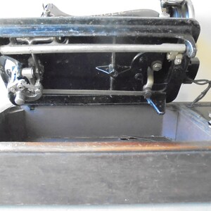 Op de afbeelding: Een zwarte Singer naaimachine met een metalen naaldplaat en een houten basis. De machine is open en de naaldplaat is zichtbaar. De machine is in goede staat en lijkt vintage te zijn.
