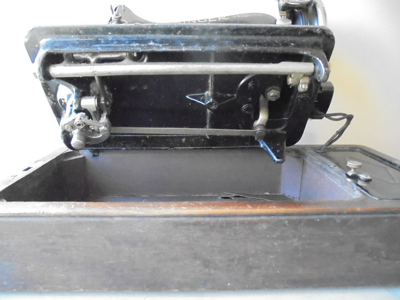 Op de afbeelding: Een zwarte Singer naaimachine met een metalen naaldplaat en een houten basis. De machine is open en de naaldplaat is zichtbaar. De machine is in goede staat en lijkt vintage te zijn.