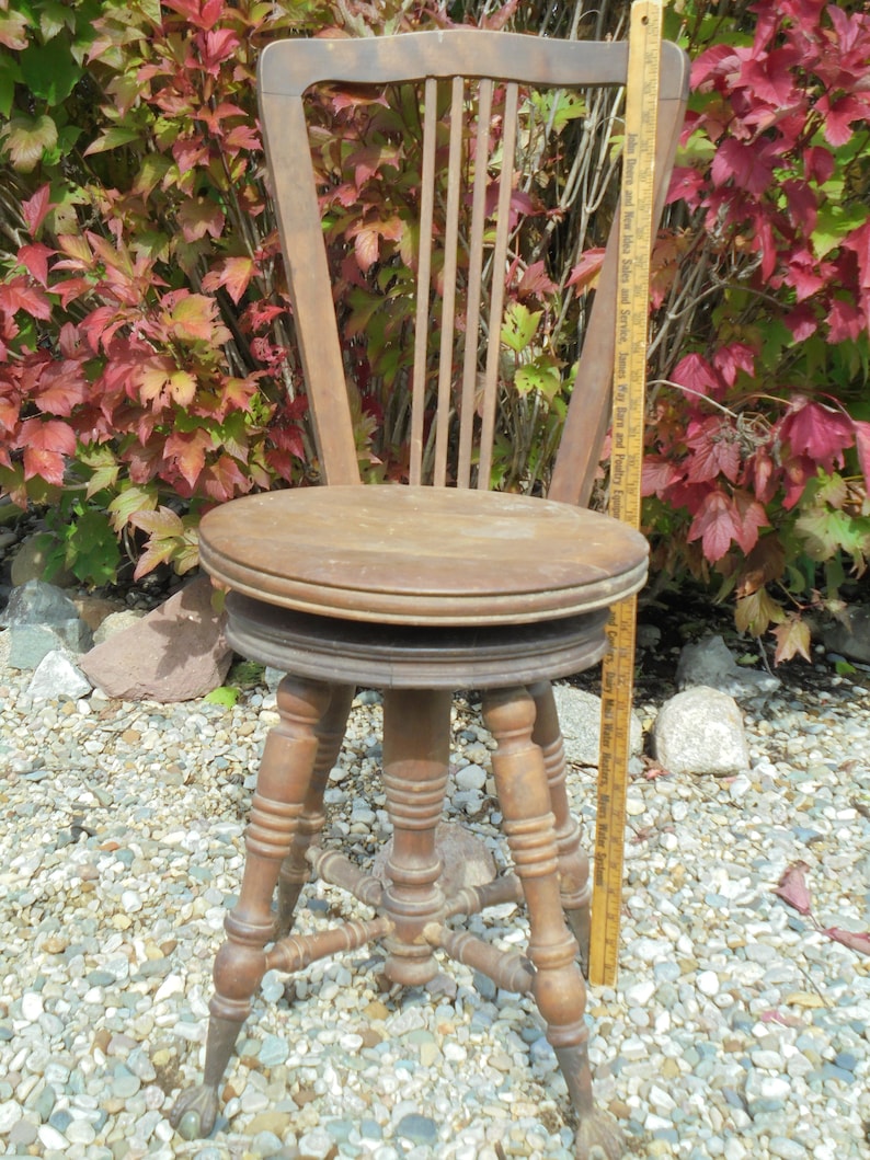 Pu&ograve; includere: Uno sgabello in legno con schienale a fuso tornito e quattro gambe tornite. Lo sgabello &egrave; dipinto di un colore marrone scuro e ha una finitura usurata. Lo sgabello &egrave; seduto su un letto di ghiaia.