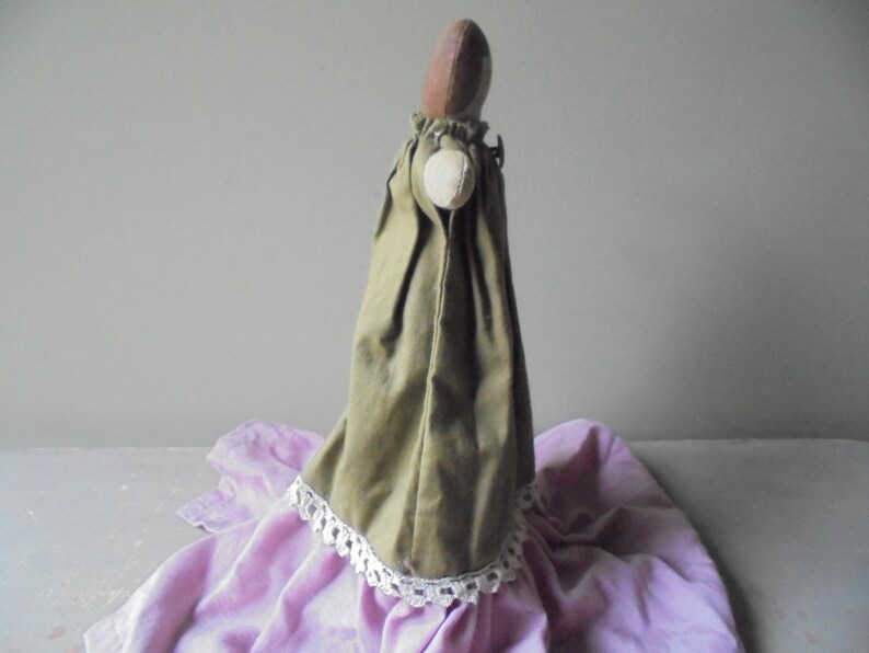 K&ouml;nnte beinhalten: Eine handgemachte Puppe, die ein gr&uuml;nes Kleid mit wei&szlig;er Spitzenborte tr&auml;gt. Die Puppe sitzt auf einem violetten Stoff.