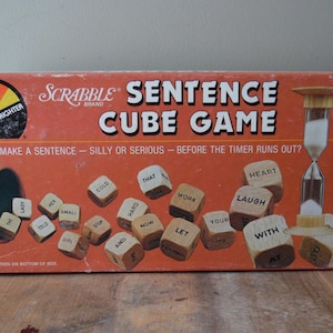 May include: Vintage Scrabble Sentence Cube Game box with word cubes and an hourglass timer. The orange box features the game title and the phrase "Can you make a sentence - silly or serious - before the timer runs out?"