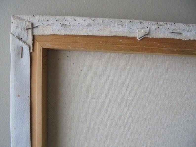 May include: Close-up of the top edge of a canvas painting. The canvas is stretched over a wooden frame and secured with staples. The canvas is white and the frame is a light brown wood.