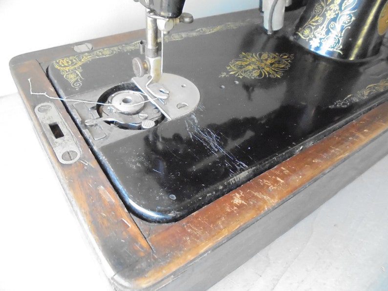 Op de afbeelding: Een vintage zwarte naaimachine met gouden accenten en een houten basis. De machine heeft een spoelwinder en een naaldinvoer.
