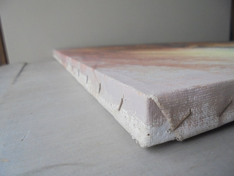 May include: Close-up of the edge of a canvas painting. The canvas is stretched over a wooden frame and secured with staples. The canvas is a light beige color and the staples are silver.