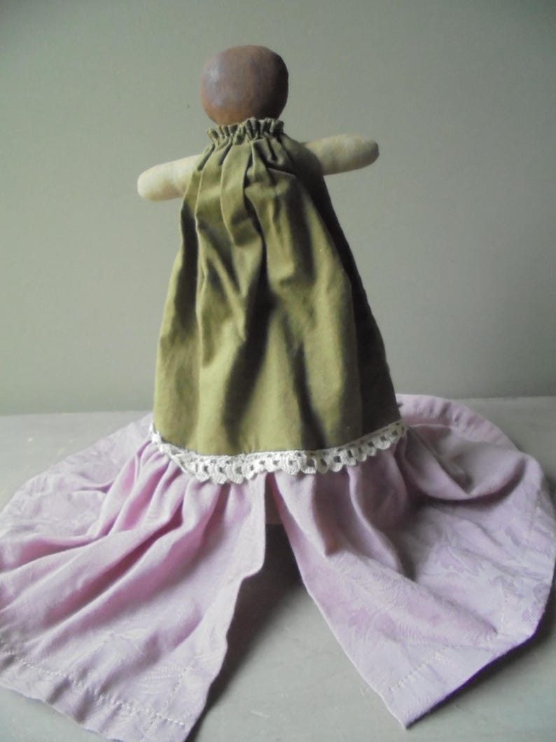 K&ouml;nnte beinhalten: Eine handgemachte Puppe mit einem braunen Kopf und einem gr&uuml;nen Kleid mit einer wei&szlig;en Spitzenborte. Die Puppe tr&auml;gt einen rosa Rock.
