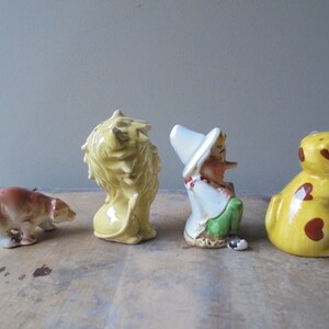 May include: A collection of four ceramic figurines: a brown bear, a yellow lion, a gnome, and a yellow dog with brown spots. The figurines are arranged in a row, each with unique details and colors.