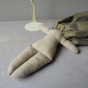 K&ouml;nnte beinhalten: Eine handgemachte Stoffpuppe mit einem beigefarbenen Stoffk&ouml;rper und Gliedma&szlig;en. Die Puppe liegt auf einer hellgrauen Oberfl&auml;che.