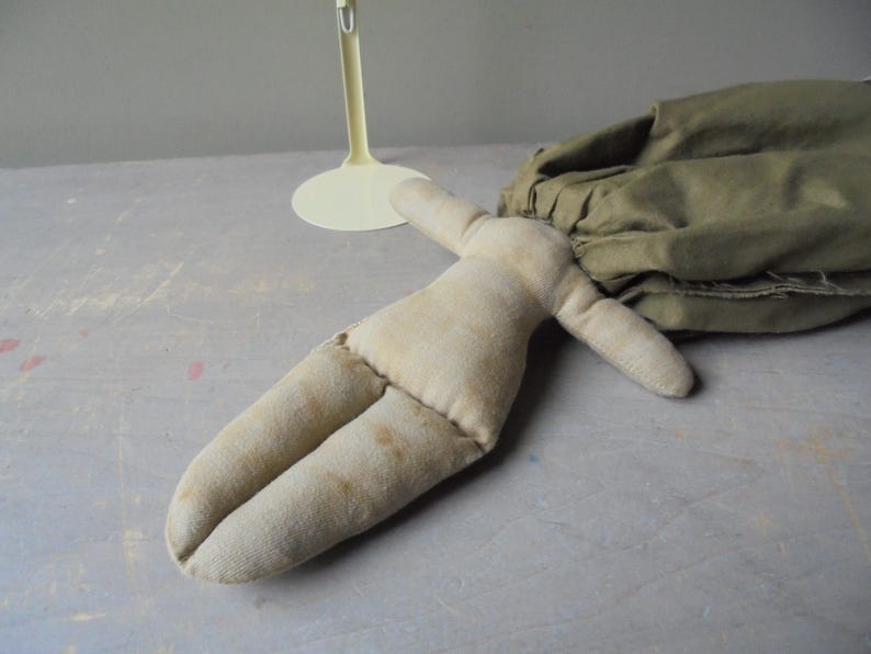 K&ouml;nnte beinhalten: Eine handgemachte Stoffpuppe mit einem beigefarbenen Stoffk&ouml;rper und Gliedma&szlig;en. Die Puppe liegt auf einer hellgrauen Oberfl&auml;che.