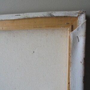 May include: Close-up of the back of a stretched canvas painting. The canvas is white and has a wooden frame. The canvas is stapled to the frame.