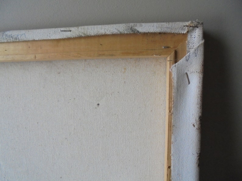 May include: Close-up of the back of a stretched canvas painting. The canvas is white and has a wooden frame. The canvas is stapled to the frame.