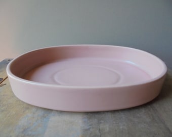 May include: A pale pink oval ceramic dish with a slightly raised rim and a smooth, glossy finish.