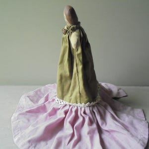 K&ouml;nnte beinhalten: Eine handgemachte Stoffpuppe, die ein gr&uuml;nes Kleid mit wei&szlig;er Spitzenborte und einen rosa Rock tr&auml;gt.