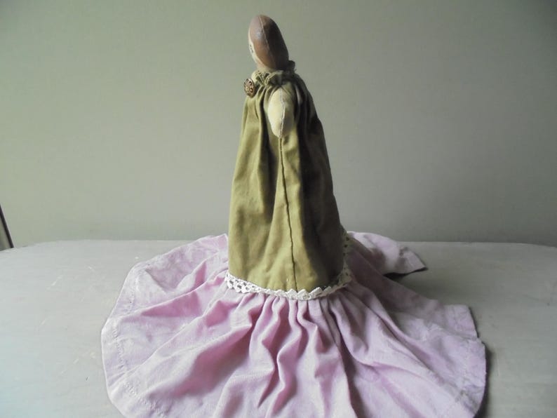 K&ouml;nnte beinhalten: Eine handgemachte Stoffpuppe, die ein gr&uuml;nes Kleid mit wei&szlig;er Spitzenborte und einen rosa Rock tr&auml;gt.