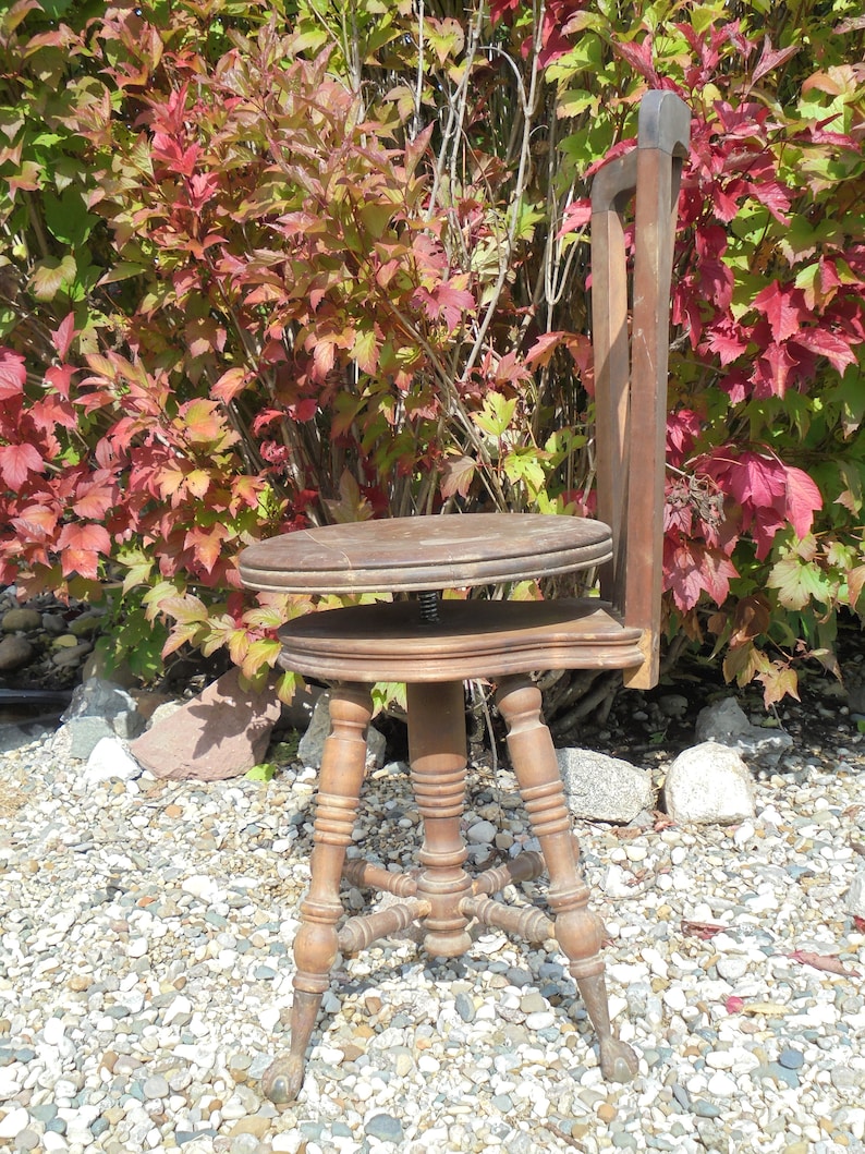 Pu&ograve; includere: Uno sgabello in legno regolabile in altezza con finitura marrone e quattro gambe. Lo sgabello &egrave; seduto su un letto di ghiaia.