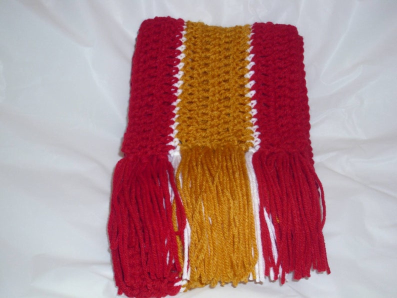 May include: A crocheted scarf with red, white, and gold stripes and tassels.