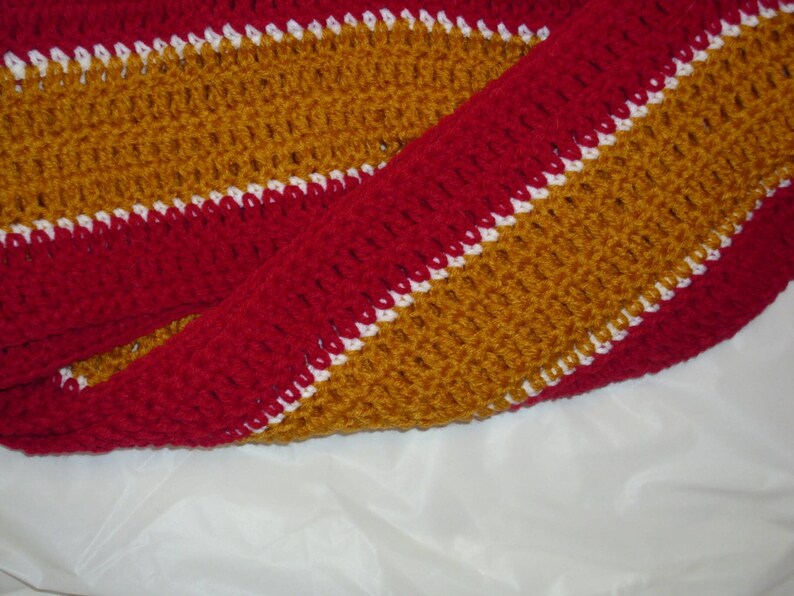 May include: A crocheted scarf with alternating stripes of red, white, and gold.