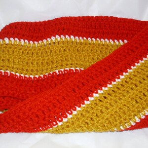 May include: A crocheted scarf with red, white, and gold stripes. The scarf is made with a simple stitch and has a soft, textured feel.