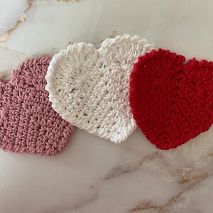May include: Three crocheted heart-shaped coasters in pink, white, and red.