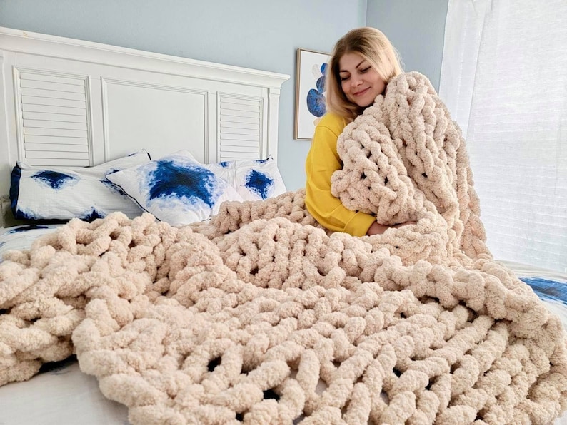 Pu&ograve; includere: Una grande coperta di maglia grossa color crema &egrave; drappeggiata su un letto con cuscini a motivi blu e bianchi. La coperta &egrave; realizzata in filato spesso e morbido e ha una sensazione rilassata e accogliente.