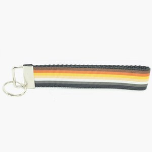 May include: A black key chain with a rainbow stripe pattern in brown, orange, yellow, white, gray, and black. The key chain has a silver key ring.