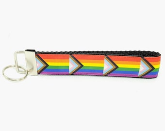 Könnte beinhalten: Ein regenbogenfarbener Schlüsselanhänger mit einem schwarzen Band und einem silbernen Schlüsselring. Das Regenbogenmuster zeigt eine Reihe von Dreiecken mit einem weißen und braunen Dreieck in der Mitte jedes Regenbogenstreifens.
