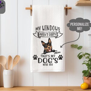 May include: White waffle-weave kitchen towel with a dog graphic and the text "MY WINDOWS AREN'T DIRTY THAT'S MY DOG'S NOSE ART". The towel is hanging on a wooden rod. A personalized name is below the dog.