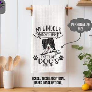 May include: White waffle-weave kitchen towel with a black and white Border Collie illustration. Text reads "MY WINDOWS AREN'T DIRTY" above the dog, and "THAT'S MY DOG'S NOSE ART" below. Includes paw prints and the name "Ethan".