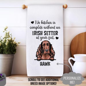 May include: White waffle-weave kitchen towel with a brown Irish Setter illustration and the text "No kitchen is complete without an Irish Setter at your feet." The dog's name, "Hawk," is below. A wooden rod holds the towel.