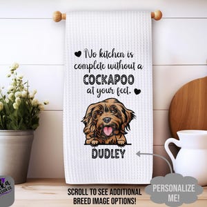 May include: White kitchen towel with a brown and white Cockapoo dog illustration. The text reads "No kitchen is complete without a Cockapoo at your feet." The dog's name is Dudley.