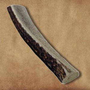 May include: A long, light brown antler dog chew with a dark brown, textured surface.